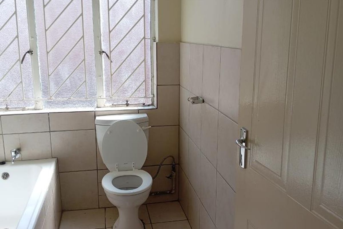A dated bathroom featuring a standard bathtub, toilet, and tiled finishes, requiring cosmetic updates to improve its overall condition and appeal.