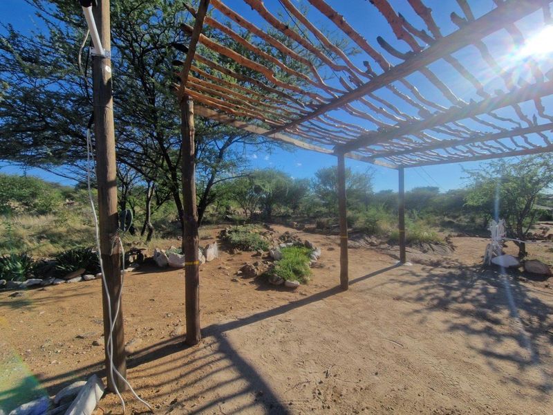 An outdoor patio area featuring a rustic wooden pergola structure set within a natural, landscaped garden environment.