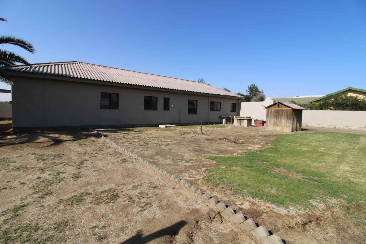 Rear view of the property featuring a large backyard, brick boundary wall, and a built-in outdoor braai area.