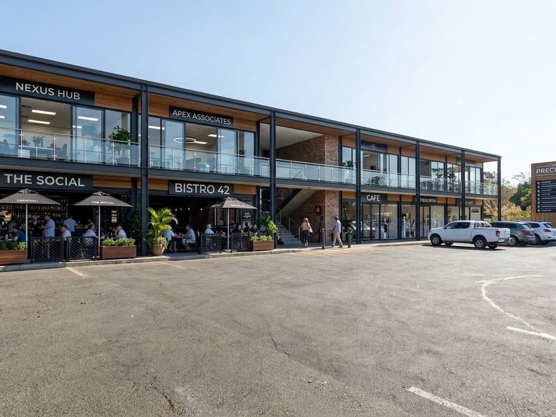 Modern mixed-use commercial building featuring a steel and glass facade, upper-level balconies, and a paved parking area with established retail and office tenants.