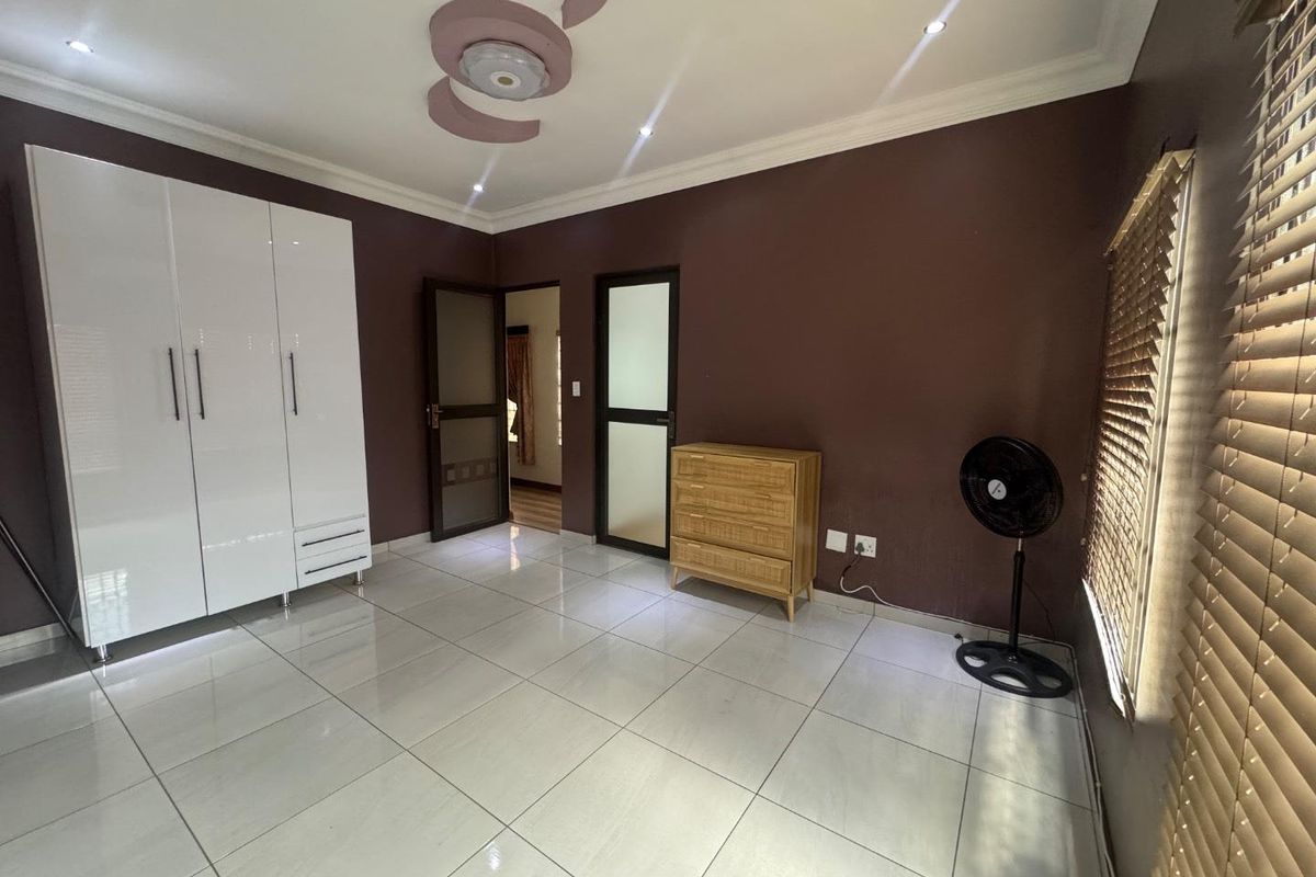 A bedroom featuring glossy tiled floors, a large white built-in wardrobe, decorative ceiling detailing, and dark accent walls with venetian blinds.