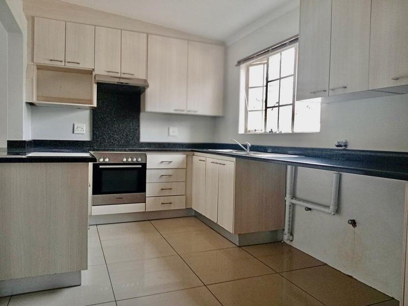 A functional kitchen featuring light-toned cabinetry, dark granite countertops, built-in oven, extractor fan, and tiled flooring with an open space for appliances.