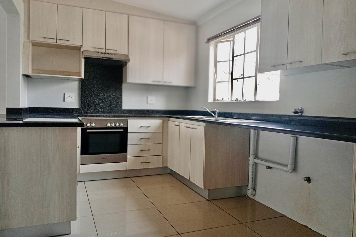 A functional kitchen featuring light-toned cabinetry, dark granite countertops, built-in oven, extractor fan, and tiled flooring with an open space for appliances.