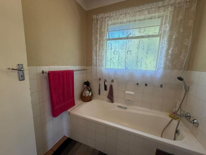 A functional bathroom featuring a built-in bathtub with a handheld shower mixer and tiled splashback, offering a classic layout ready for modern updates.