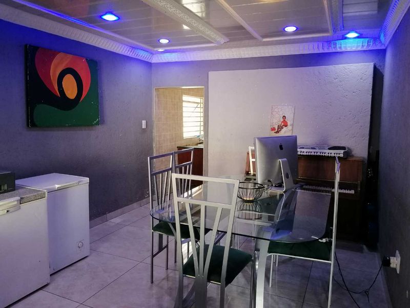 A living area featuring tiled flooring, textured walls, and a coved ceiling with integrated recessed lighting, providing access to an adjacent kitchen space.