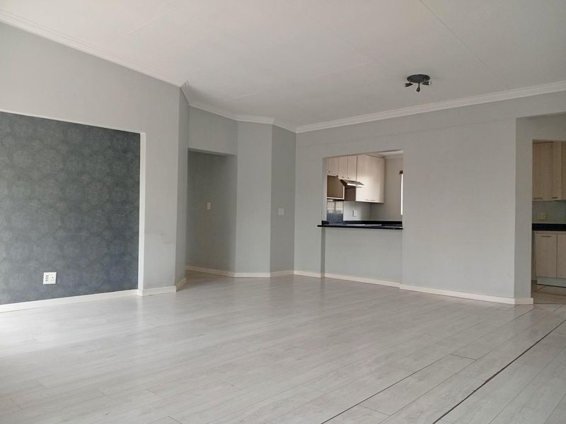 Spacious open-plan living area featuring light laminate flooring, coved cornicing, and a convenient pass-through window connecting to the kitchen.