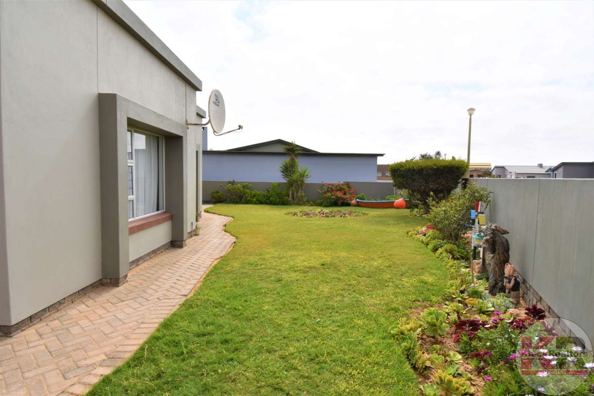 A well-maintained rear garden featuring a paved walkway, manicured lawn, and established perimeter landscaping along the boundary wall.