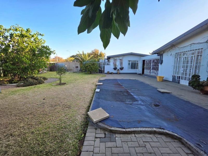 Rear garden area featuring a swimming pool with a cover, paved patio space, and established landscaping adjacent to the main house structure.