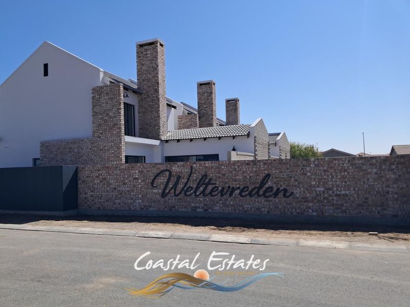 Front view of the Weltevreden townhouse complex featuring modern brick and plaster architecture with prominent chimneys and a secure boundary wall.