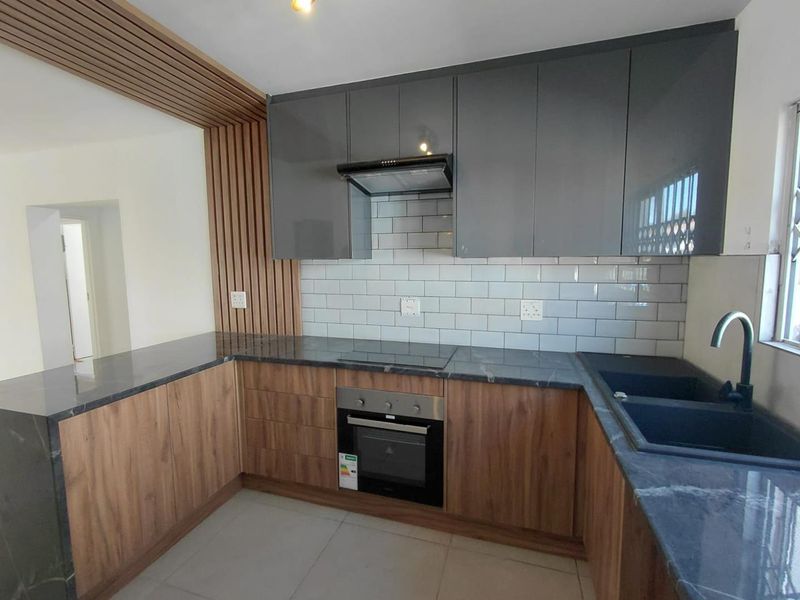 Modern kitchen featuring sleek grey and wood-grain cabinetry, stone countertops, subway tile backsplash, and integrated appliances with a stylish slatted timber accent wall.