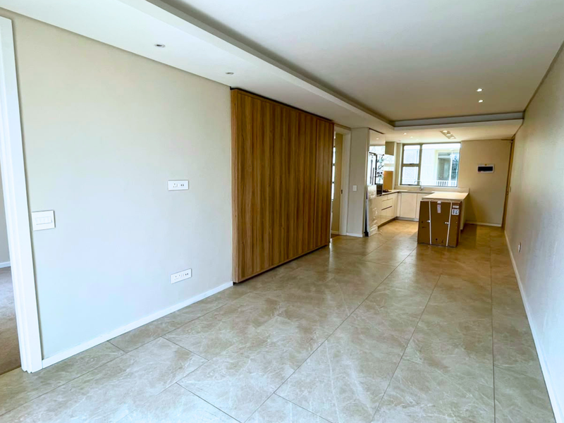 Spacious open-plan living and kitchen area featuring modern tiled flooring, recessed ceiling lighting, and sleek built-in cabinetry with a central kitchen island.