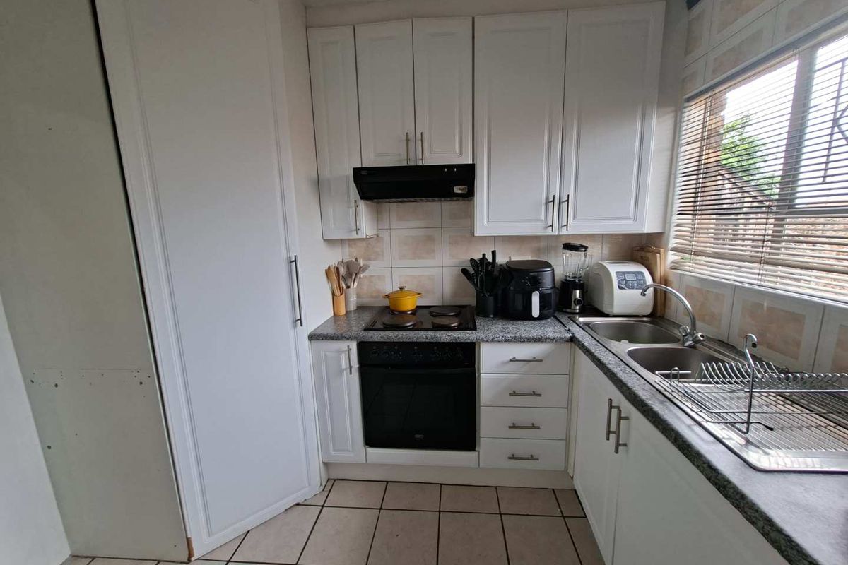 Compact kitchen featuring white cabinetry, built-in oven, electric hob, extractor fan, and a double stainless steel sink with tiled splashbacks.