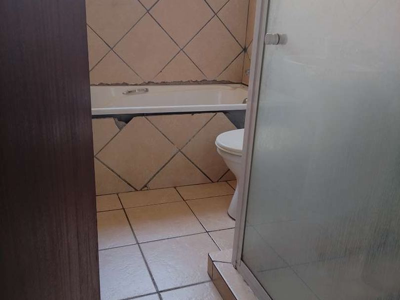 A functional bathroom featuring a bathtub, shower enclosure, and toilet, with tiled finishes requiring some maintenance and repair work.