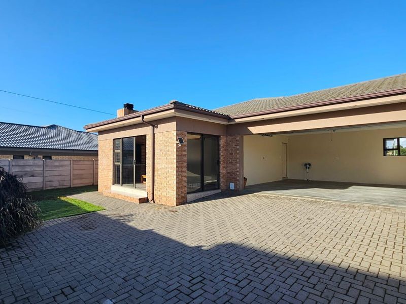 Rear view of the property featuring a paved driveway, double garage, and sliding door access to the main living area.