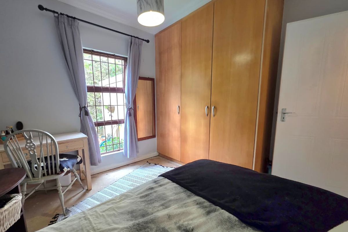 A bedroom featuring built-in wooden cupboards, a window with security bars, and neutral wall finishes.