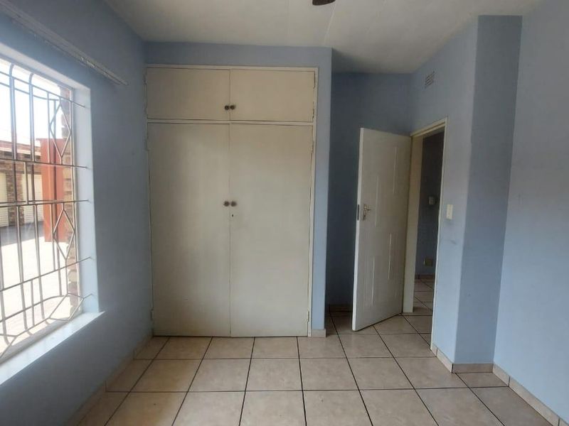 An empty bedroom featuring tiled flooring, built-in cupboards, and a window fitted with security bars.