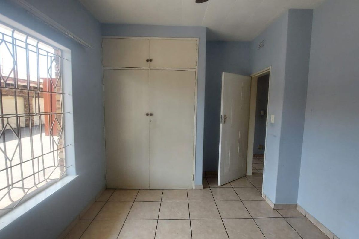 An empty bedroom featuring tiled flooring, built-in cupboards, and a window fitted with security bars.