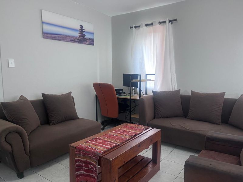 A functional living room area featuring neutral wall tones and tiled flooring, providing a comfortable space for relaxation and home office use.
