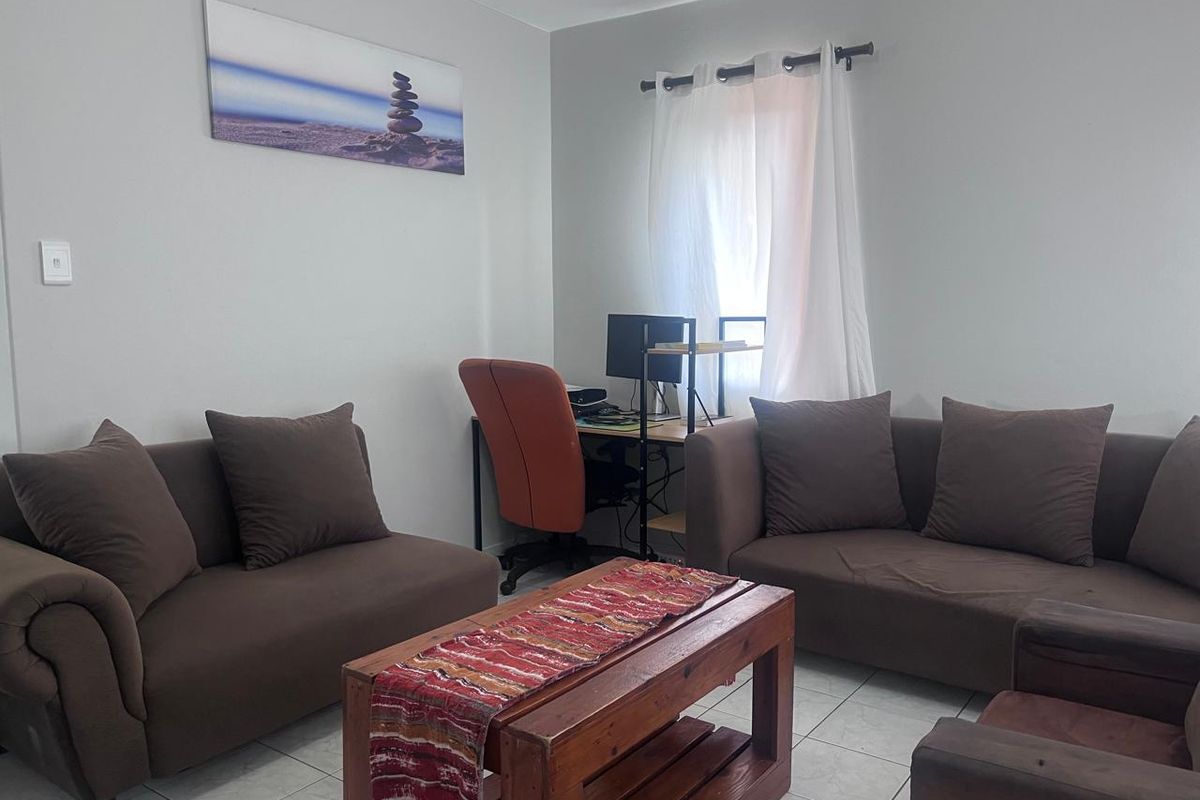 A functional living room area featuring neutral wall tones and tiled flooring, providing a comfortable space for relaxation and home office use.