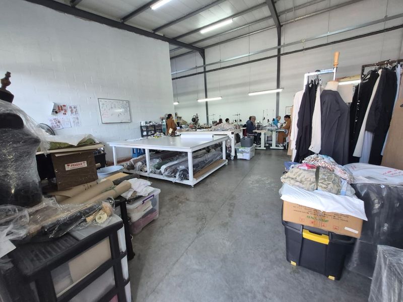 Industrial workspace featuring high ceilings with exposed steel trusses, concrete flooring, and functional strip lighting, currently utilized as a garment production area.