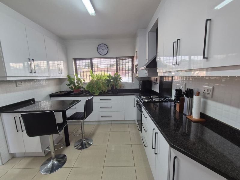 Modern kitchen featuring white high-gloss cabinetry, contrasting black granite countertops, built-in oven and hob, and tiled flooring.