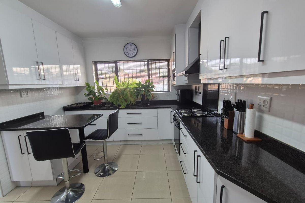 Modern kitchen featuring white high-gloss cabinetry, contrasting black granite countertops, built-in oven and hob, and tiled flooring.