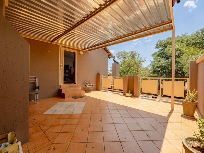 A spacious covered patio featuring tiled flooring, a corrugated metal roof, and a metal balustrade, providing an ideal outdoor entertainment area.