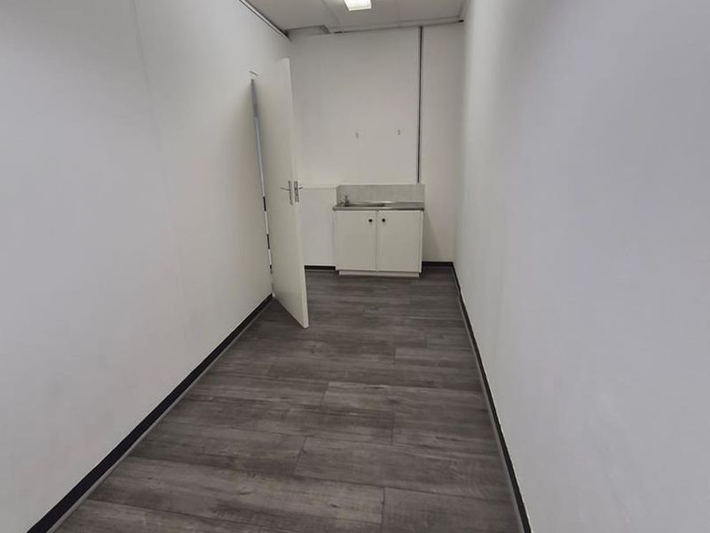 A clean, empty utility space featuring laminate flooring, a drop ceiling with integrated lighting, and a small base cabinet with a stainless steel sink.