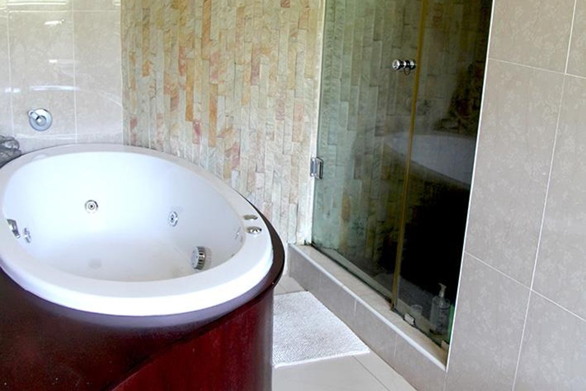 Modern bathroom featuring a built-in spa bath, a glass-enclosed shower, and a decorative stone feature wall with neutral ceramic tiling.