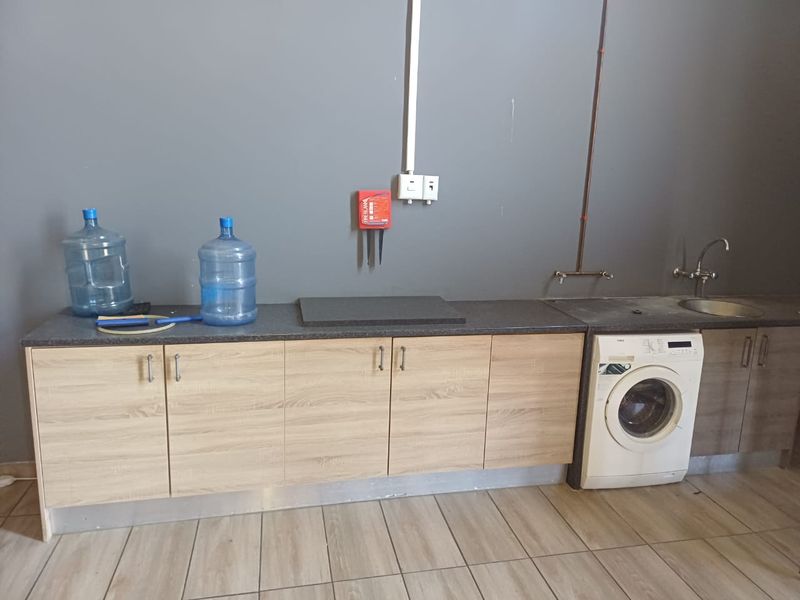 A functional laundry area featuring built-in light wood cabinetry, a dark laminate countertop, a stainless steel sink, and tiled flooring.
