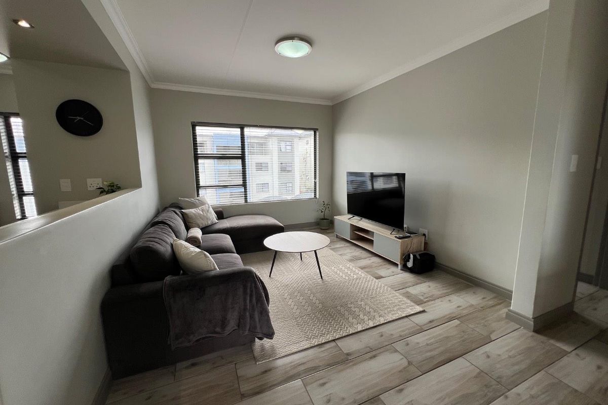 A well-maintained living room featuring neutral wall tones, tiled flooring, and large windows with venetian blinds, providing a bright and comfortable living space.