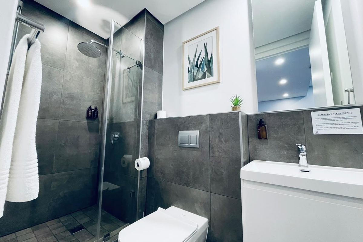 Modern bathroom featuring a walk-in shower with dark grey tiling, a wall-mounted toilet, and a sleek vanity basin with a large mirror.