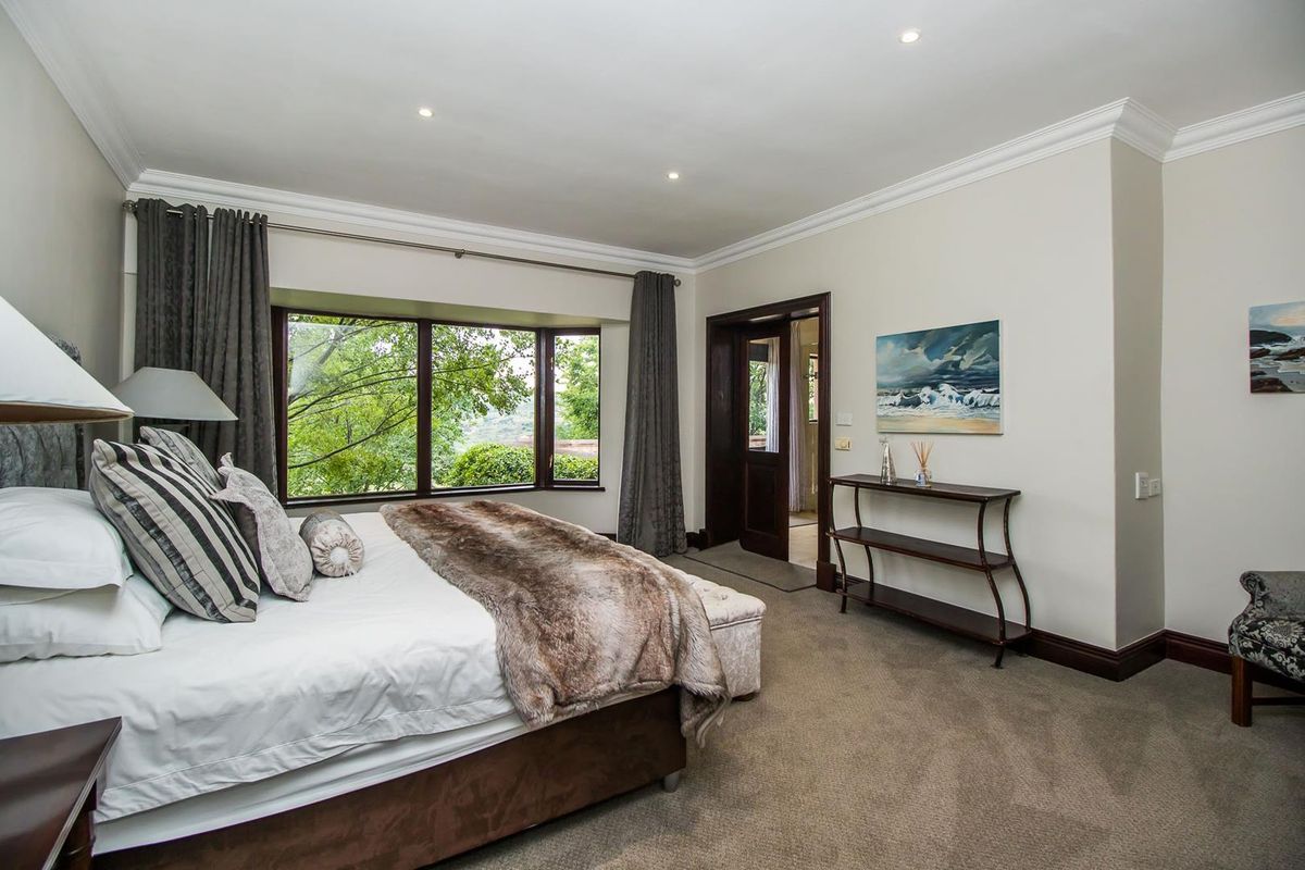 A well-maintained bedroom featuring neutral carpeting, crown molding, recessed lighting, and a large bay window overlooking greenery.