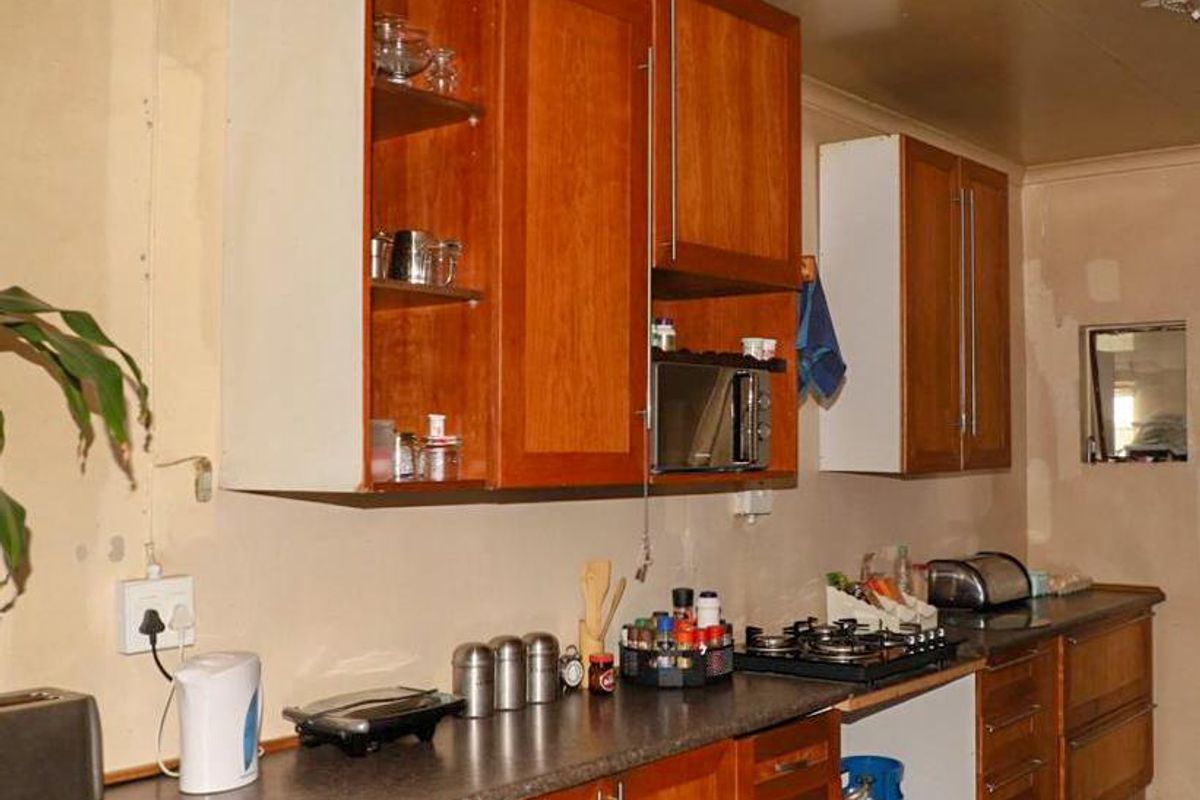 A dated kitchen featuring wooden cabinetry, a gas hob, and tiled flooring, requiring cosmetic updates and wall finishing to reach its full potential.