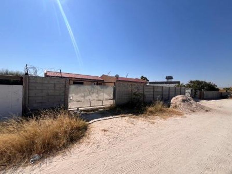 Front view of the property featuring a perimeter wall with a metal gate, razor wire security, and a tiled roof structure.