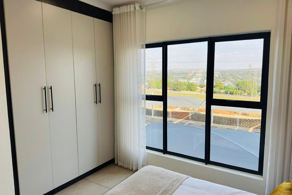A bright bedroom featuring built-in floor-to-ceiling wardrobes with modern finishes and large windows offering an expansive elevated view.