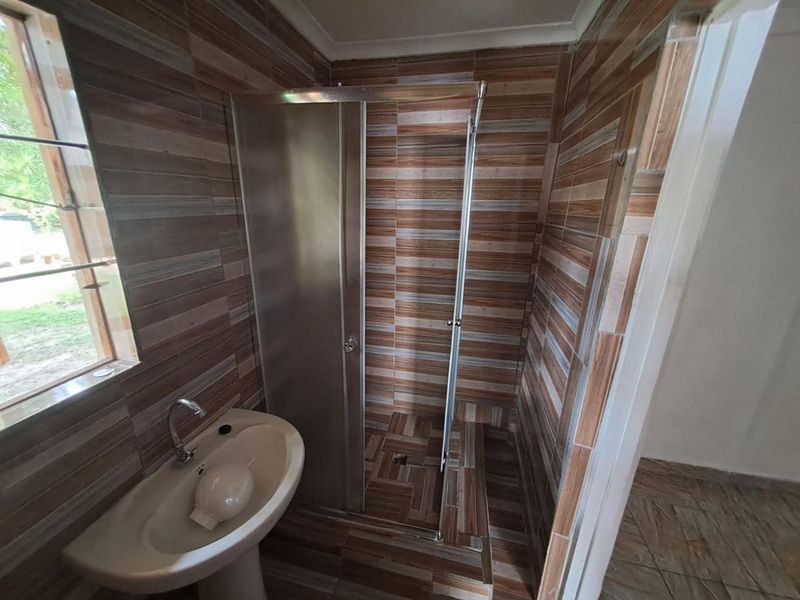 A functional bathroom featuring a pedestal basin, tiled walls and flooring, and a glass-enclosed shower stall.