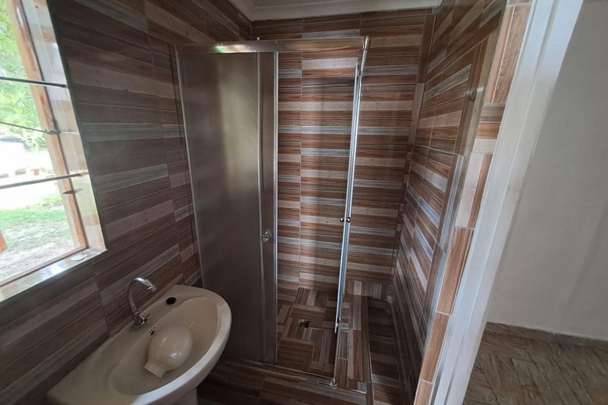 A functional bathroom featuring a pedestal basin, tiled walls and flooring, and a glass-enclosed shower stall.