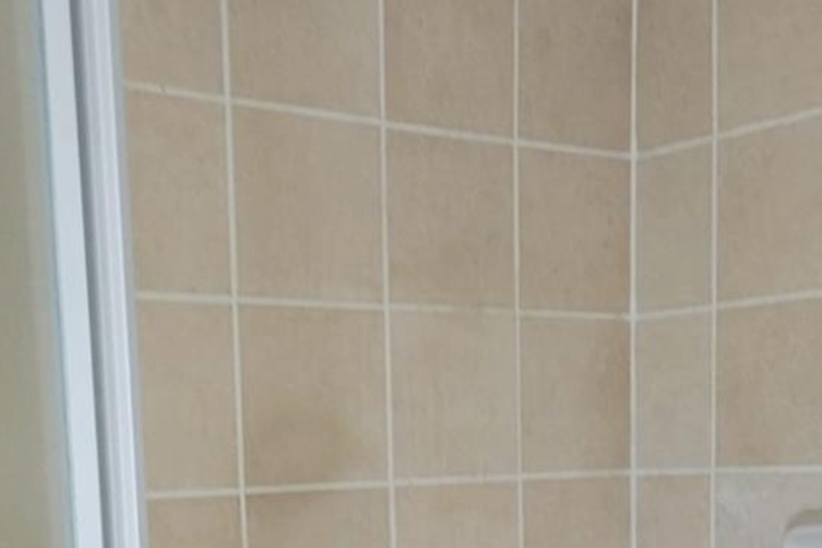 A functional shower enclosure featuring beige wall tiles, a fixed shower head, and chrome plumbing fixtures.