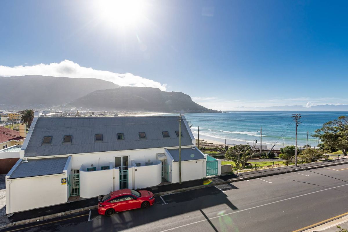 Aerial view of the property exterior, showcasing its coastal location, proximity to the beach, and surrounding mountain landscape.