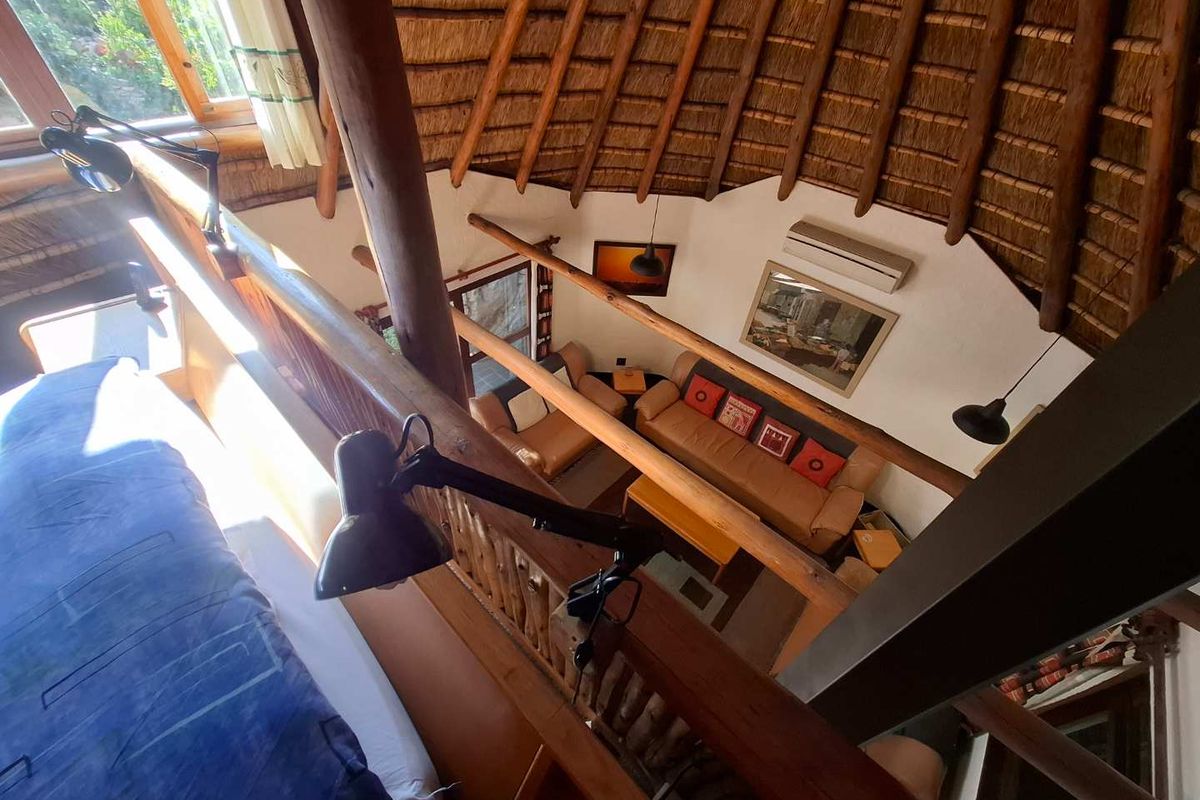 A mezzanine level overlooking a living area, featuring a traditional thatched roof, exposed timber beams, and a wooden balustrade.