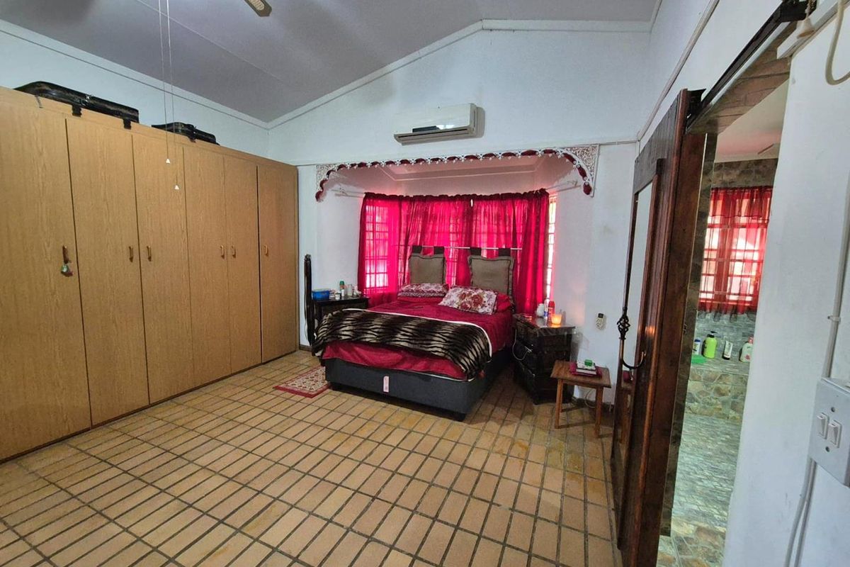 Spacious bedroom featuring built-in wooden wardrobes, vaulted ceilings, an integrated air conditioning unit, and direct access to an en-suite bathroom.
