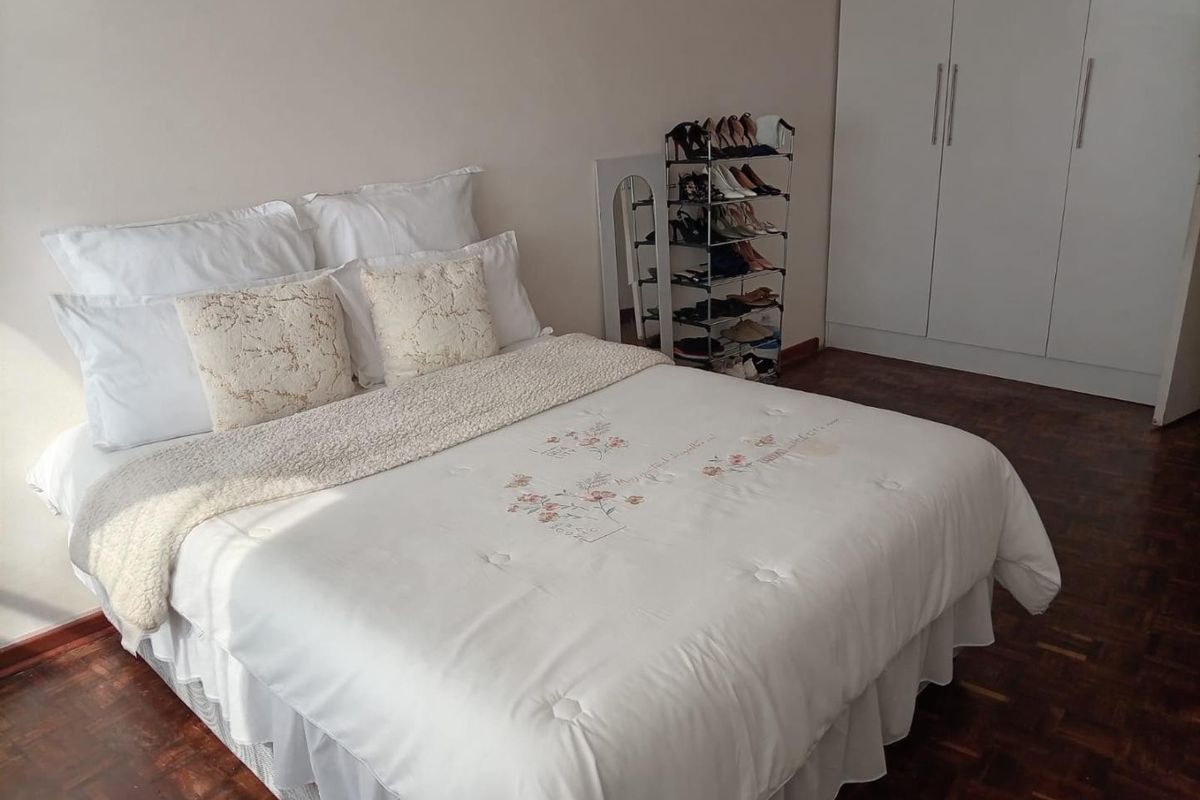 A well-maintained bedroom featuring classic parquet flooring and a functional built-in wardrobe with clean white finishes.