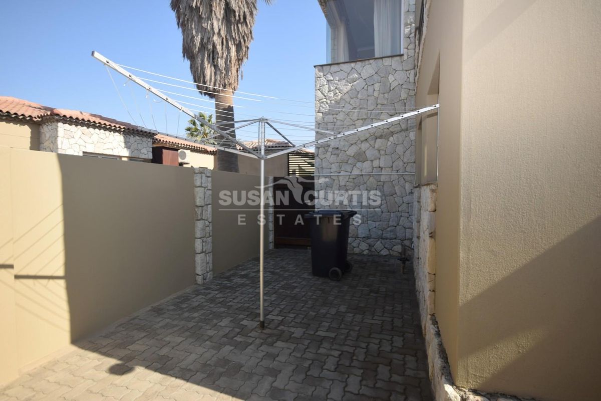 A private rear courtyard featuring stone-clad walls, paved flooring, and a functional rotary clothesline area.
