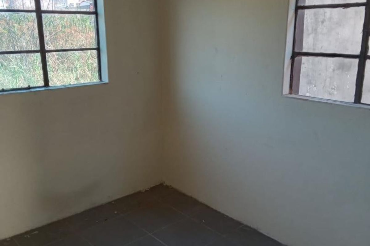 An empty bedroom featuring tiled flooring and steel-framed windows, requiring cosmetic updates and ceiling repairs.