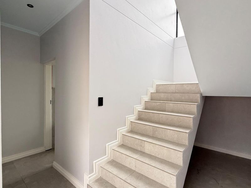A bright and modern hallway featuring a clean staircase with tiled steps and neutral wall finishes.