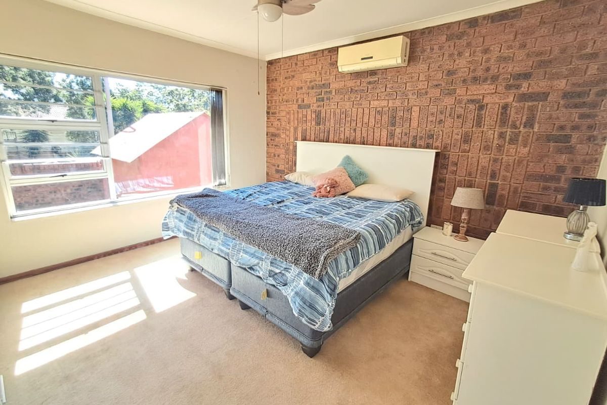 A bedroom featuring a prominent face-brick feature wall, large window for natural light, ceiling fan, and wall-mounted air conditioning unit.
