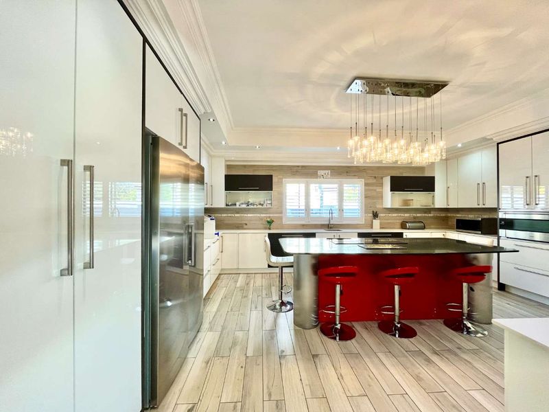Modern kitchen featuring a large central island with stone countertop, high-gloss cabinetry, integrated appliances, and stylish pendant lighting.