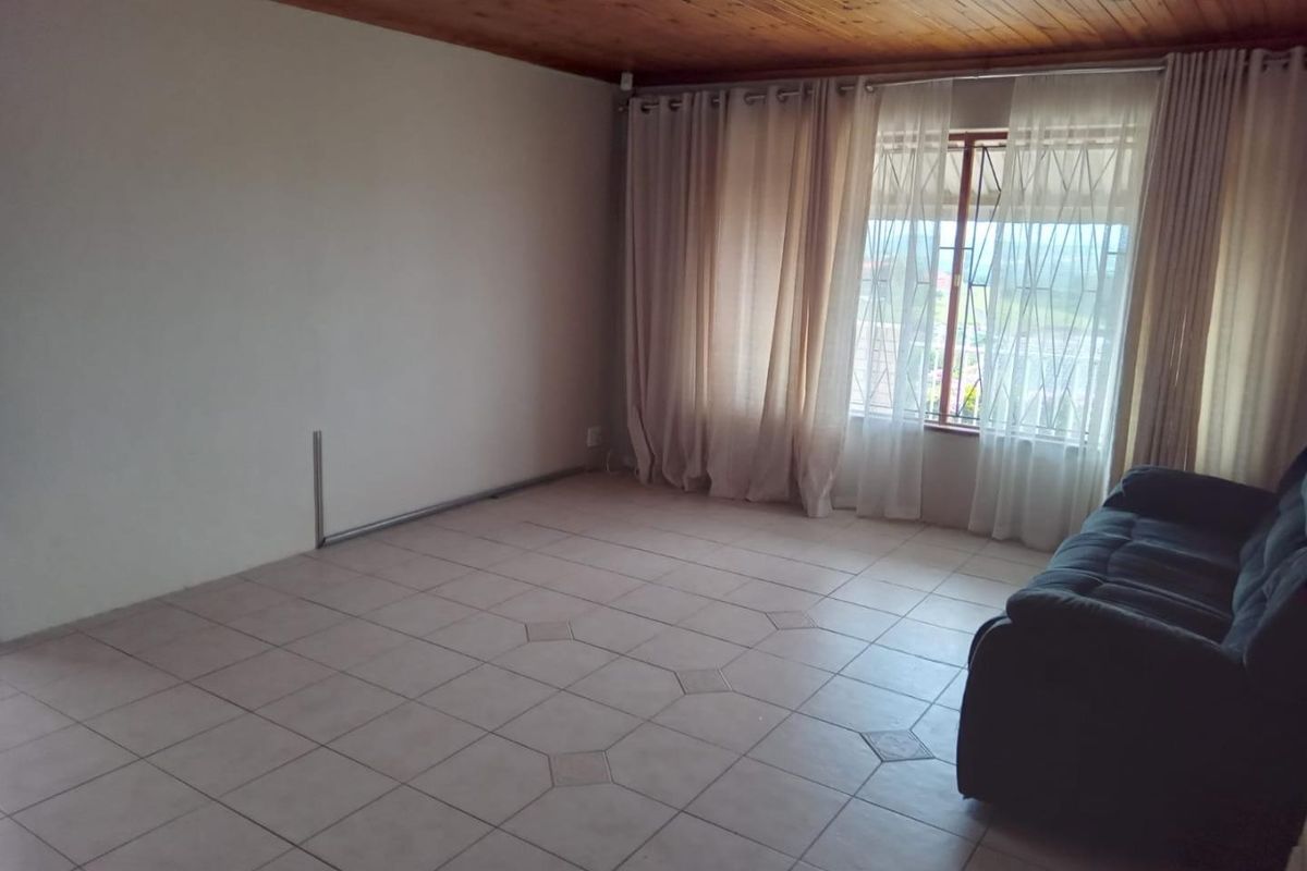 A living room featuring tiled flooring and a timber ceiling, with a window fitted with security bars and curtains.