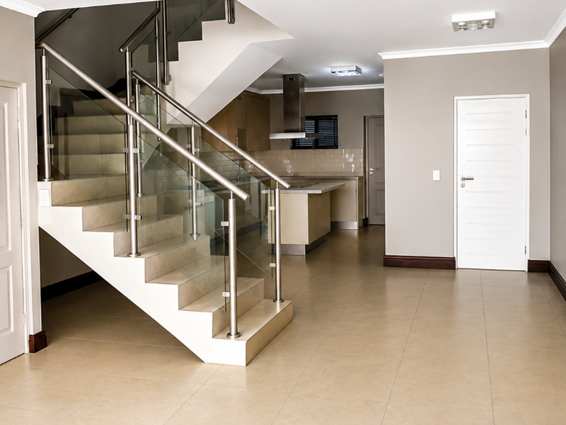 Spacious open-plan living area featuring a modern staircase with glass balustrades and a sleek, well-appointed kitchen in the background.
